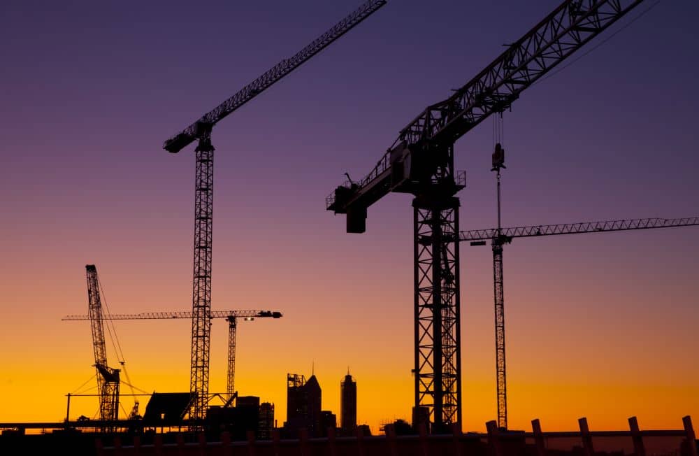 Silhouette of construction cranes with sunset on the background.